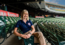 a woman in professional clothing sits at a baseball stadium